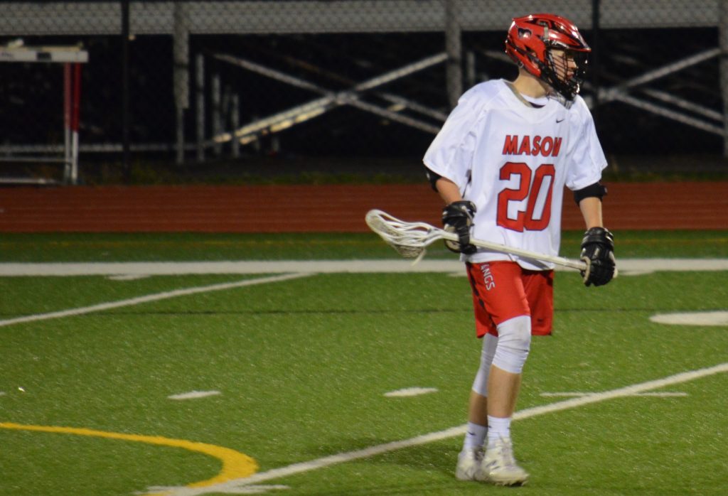 Lacrosse player holds his lacrosse stick with a ball on a turf field. 