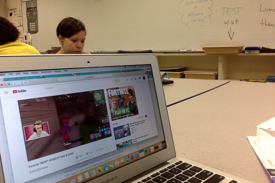 A computer on a desk in a classroom playing a Fortnite photo.