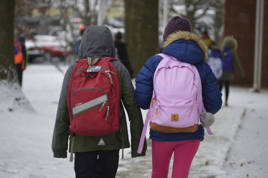 Two students in coats walk in the snow