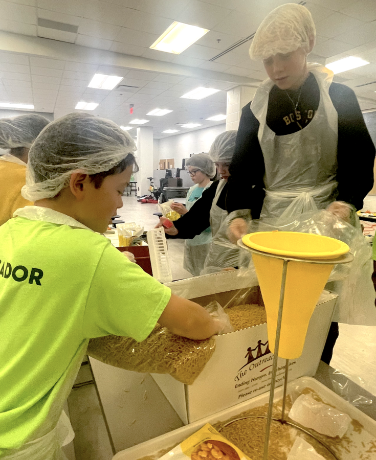 Middle school ambassador Noah Mayer (left) helps scoop macaroni during the MEH meal packing event. (Photo courtesy of  Meridian Give Day)