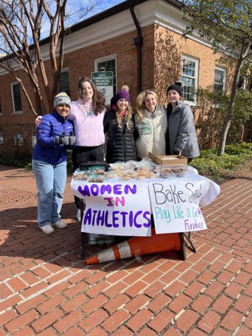 [Left to Right] Sophomore Joyce Tadesse Kassa, juniors Maureen Tremblay and Reese Davis, sophomore Jenna Hall, and junior Ivy Anderson smile behind their bake sale stand at the Falls Church Farmers Market. (Photo courtesy of Ivy Anderson)