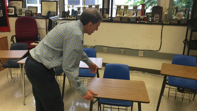 A teacher moves a desk across the classroom.