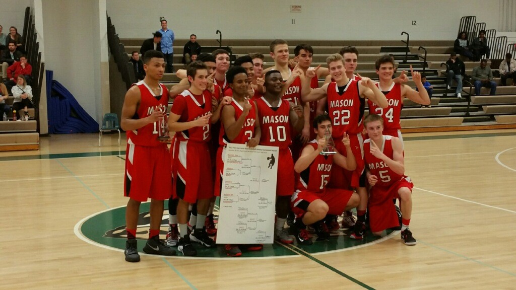 The boys varsity team poses with their trophy and tournament chart from a tournament.