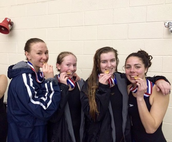 Mustang girl swimmers bite their medals after winning their relay.