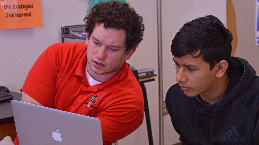 Mr. Ryan Larcamp (left) and Bikash Shahi, Senior (right) work on Shahi’s homework assignment, assigned through Schoology and to be completed using the laptop. Teachers assign homework through Schoology, which students access through the laptops and often complete using the laptops. (Photo credit to Eric Clinton)