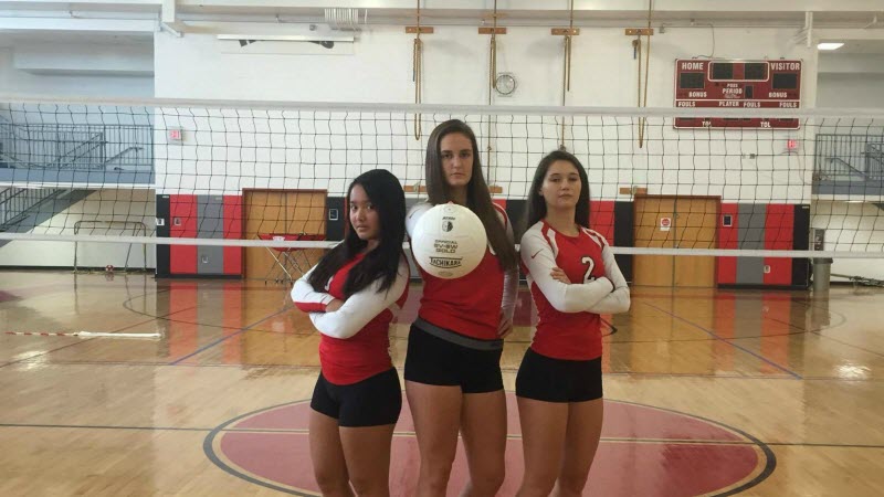 Three volleyball players holding a volleyball as they pose for the picture.