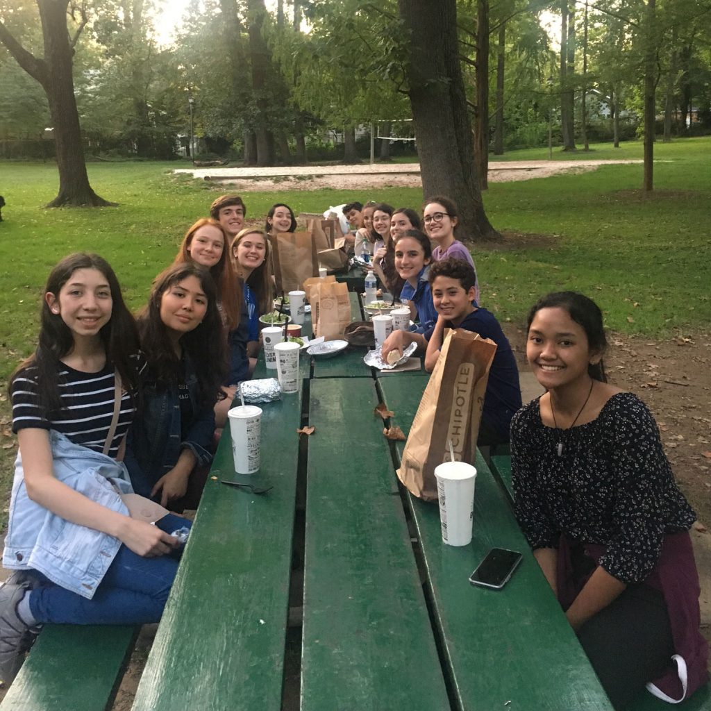 A group of students eating at a picnic table at a park.