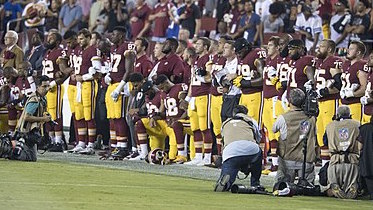 NFL players kneel and stand on the sidelines.