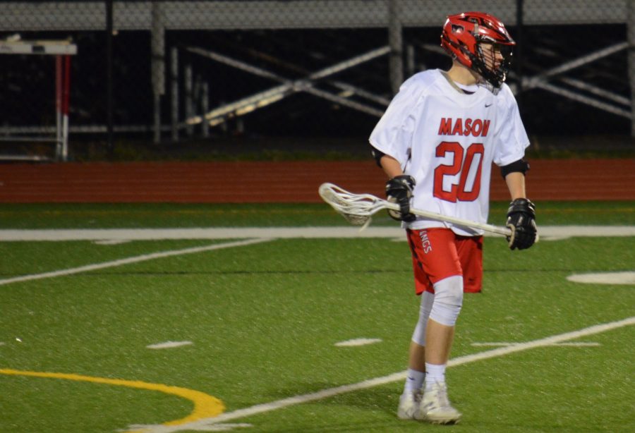 Lacrosse player holds his lacrosse stick with a ball on a turf field.