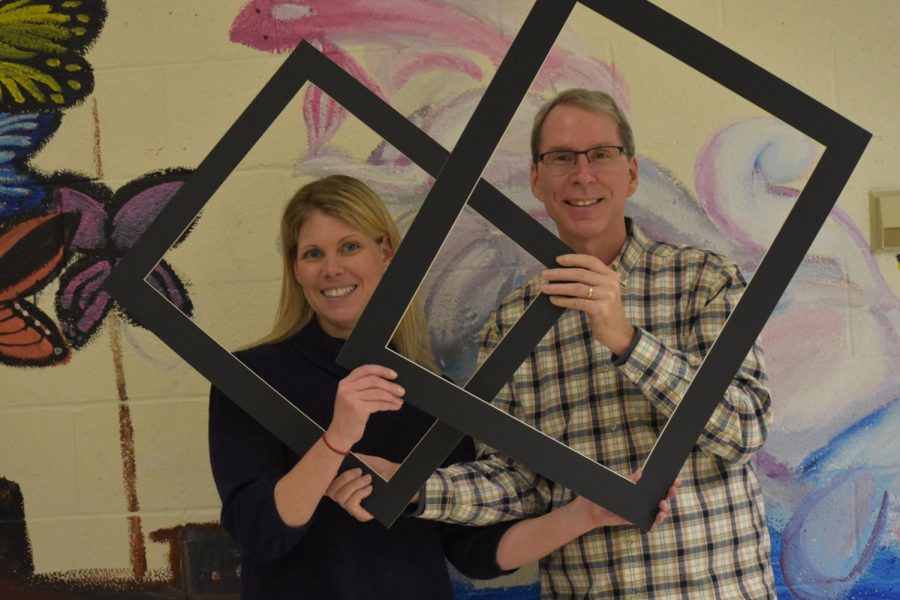 A man and woman pose for a photo holding black frames.