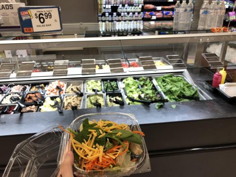 hand holding salad in front of salad bar