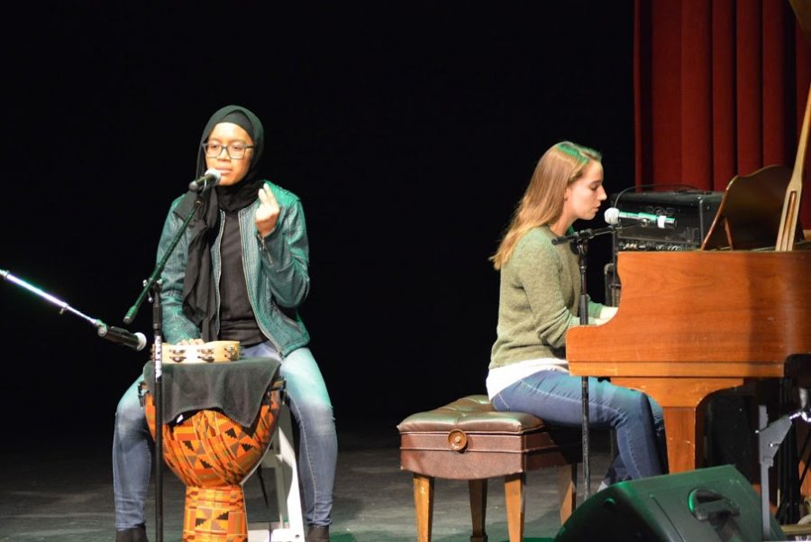 two+students+on+stage+perform+at+the+JV+show.+One+is+sitting+and+playing+a+drum%2C+and+a+second+is+behind+her+playing+piano.