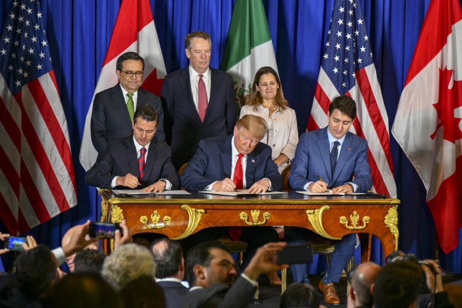 Donald Trump, Enrique Peña Nieto, and Justin Trudeau sign the USMCA as reporters and aids look on.