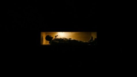 A shadowy figure lays in a coffin. 