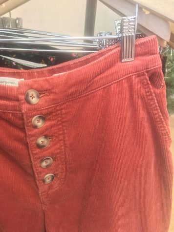 Close up photo of red corduroy pants with brown buttons hanging on a rack.