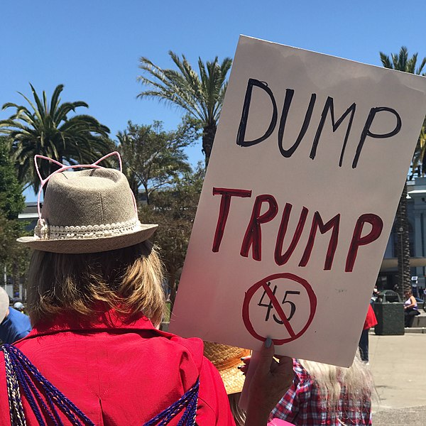A woman holds a sign reading “Dump Trump” at a rally for President Donald Trump’s impeachment.