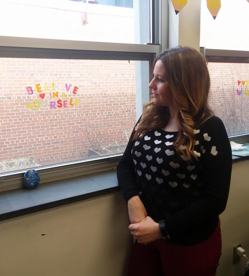 Ms. Hoffman stands and pensively looks out a window, stickers spelling out “Believe in yourself” stuck to the glass.