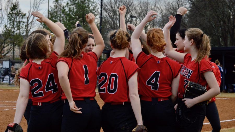 The Varsity Softball team stands in a circle and put their hands up as a cheer.