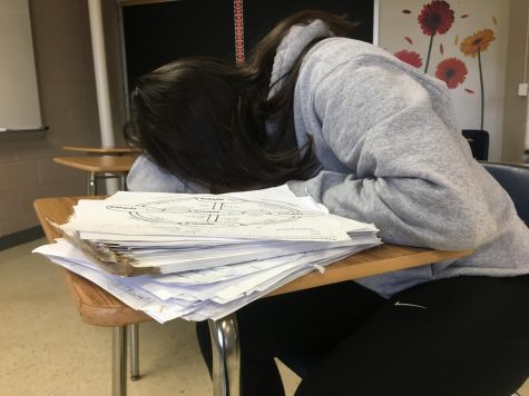 A student puts her head on a desk with papers.