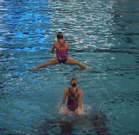 Synchronized swimmers perform a lift where they throw one girl into the air.