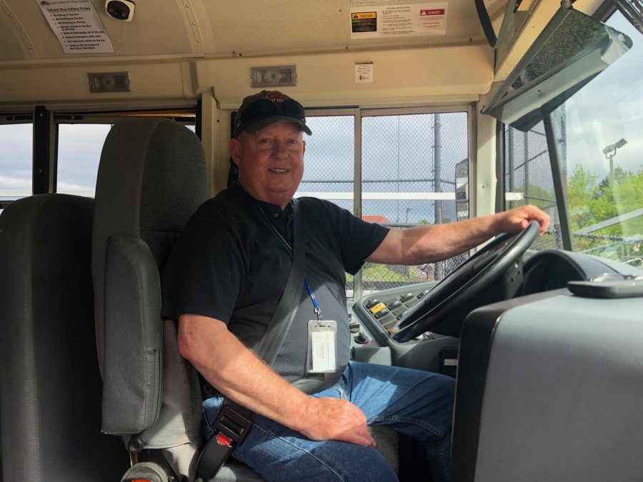 A man smiles in the driver seat of a school bus.