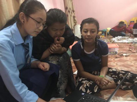 Three girls sit around computer.