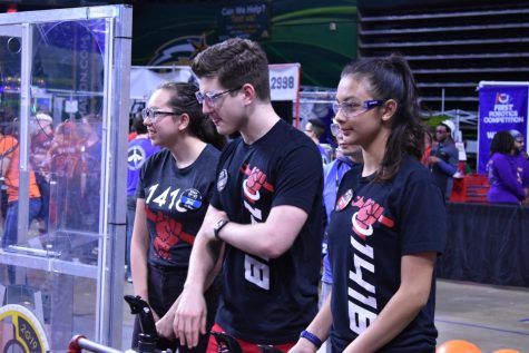 Three students stand and look to the left in a gym at a robotics tournament.