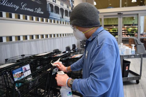 A Harris Teeter employee wipes down a shopping cart with disinfectant spray and a cloth