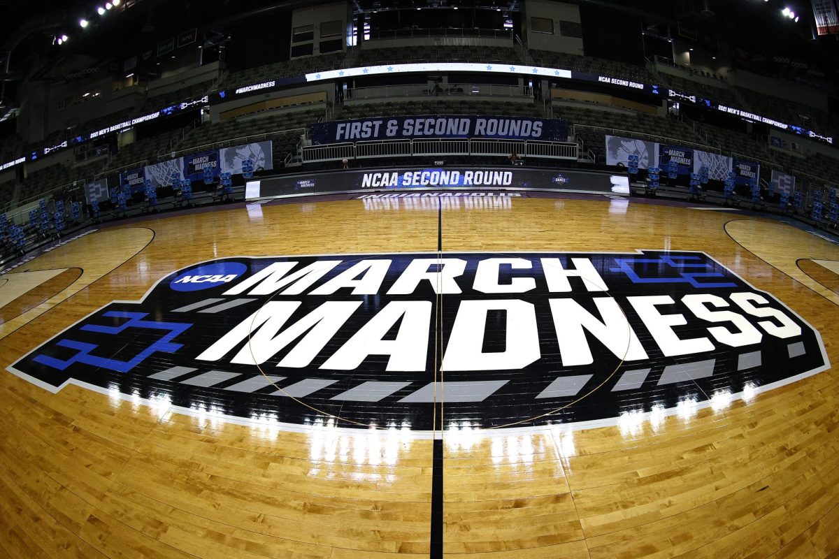 March Madness logo on the floor of a basketball stadium (Photo via Bleacher Report)