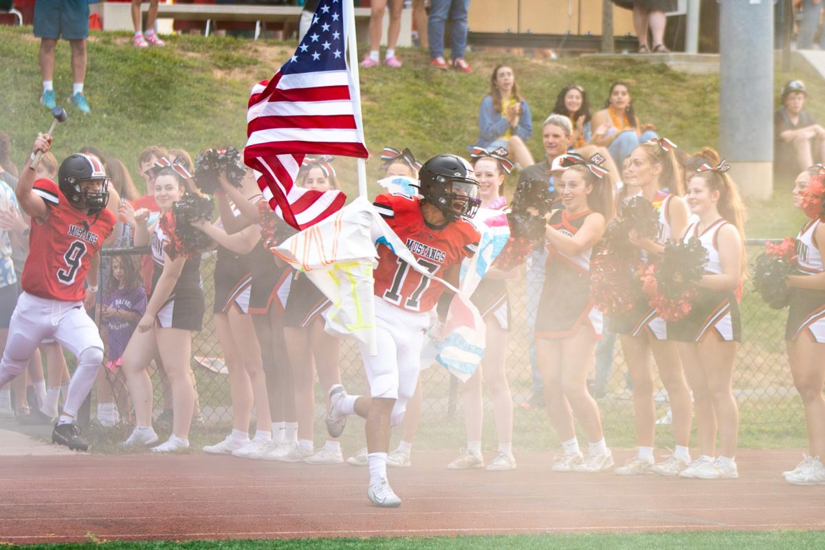 Senior Junior Martinez leads his team out of the tunnel, holding a flag, to kick off the game. (Photo by Ryan Degnan)