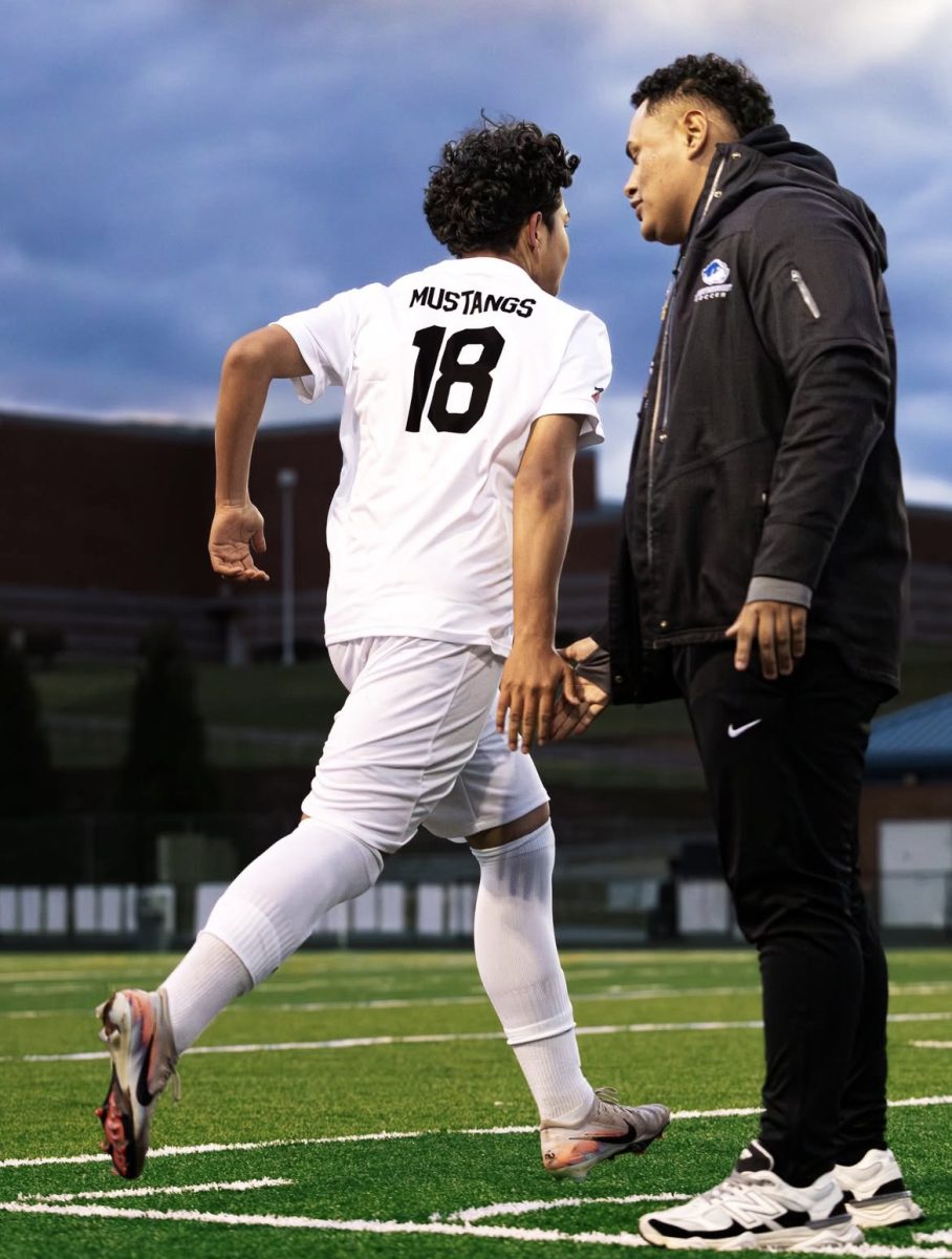Sophomore Andre Cardona runs out onto the field, with encouragement from head coach Ronald Cruz-Rivas. (Photo courtesy of Paul Meade)